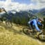 Zwei Mountainbiker IN Saalbach auf einer Abfahrt in den Alpen mit Bergpanorama im Hintergrund.